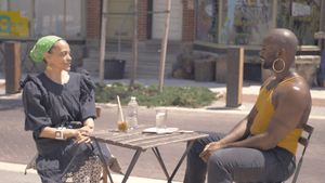 Rucker sits across from Temple outside at a small wooden table.