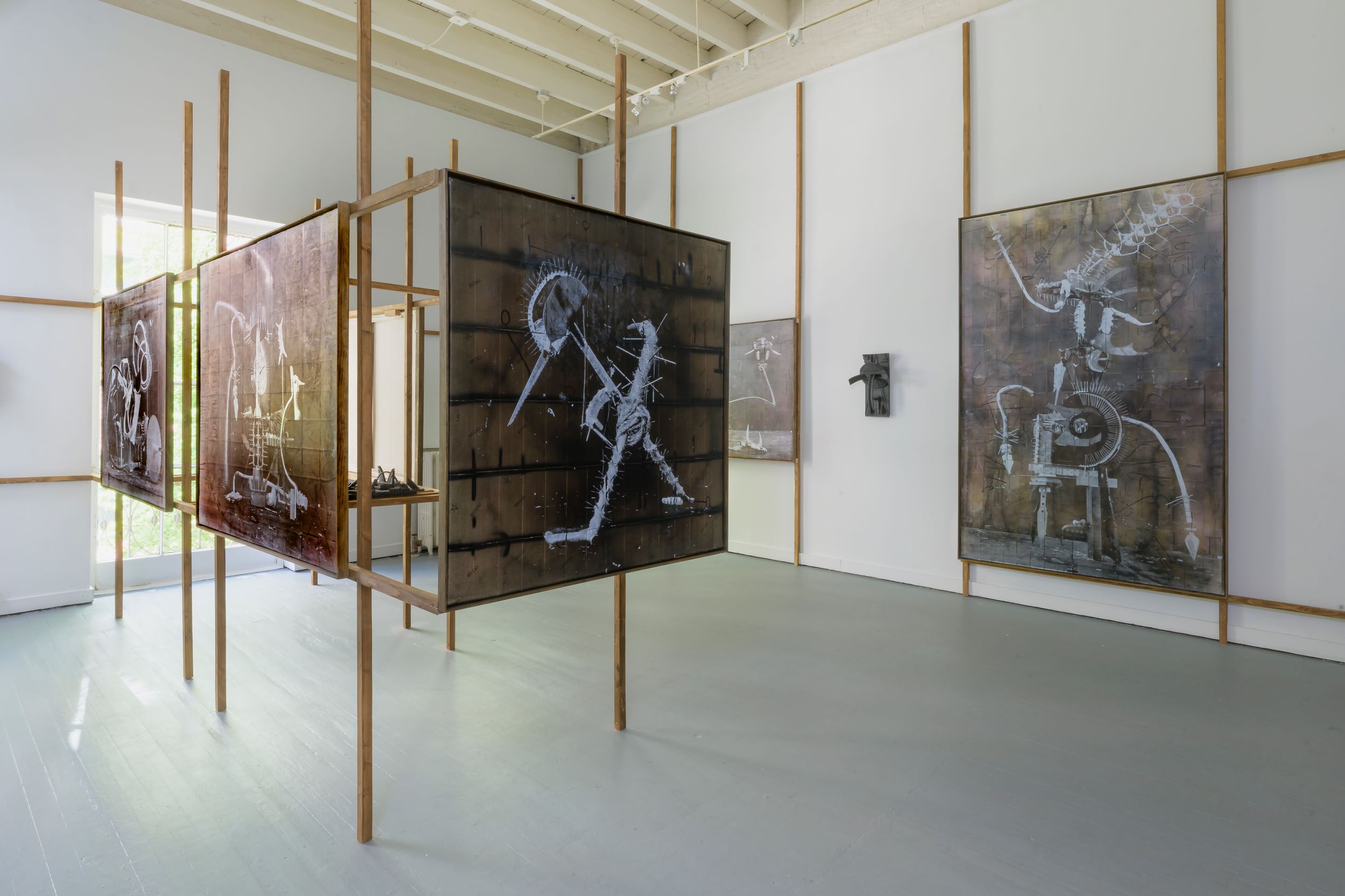 In an airy white gallery, large rectangular brown-and-white prints show vaguely anthropomorphic or animalistic machines.