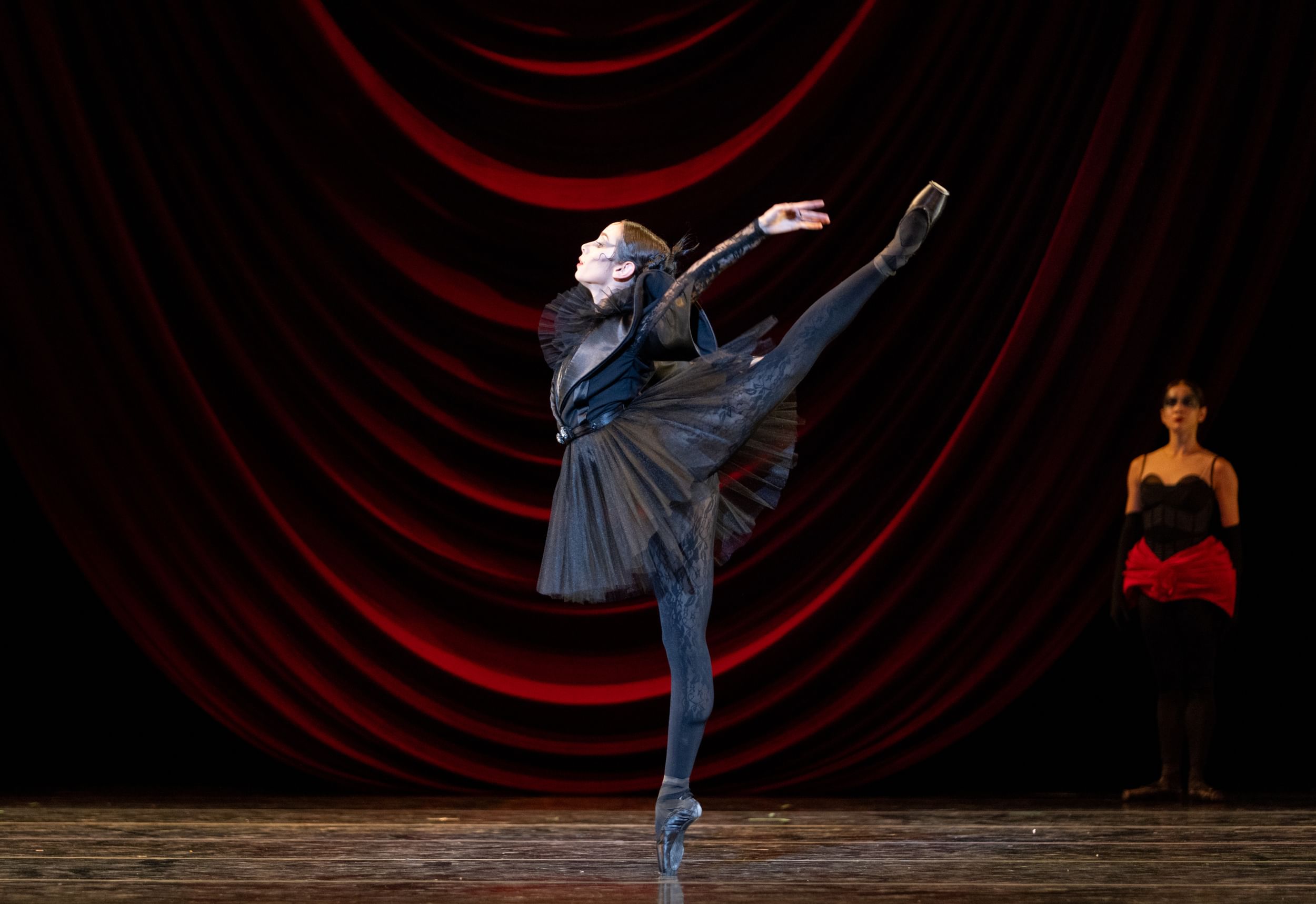 Golz, in a spooky, fantastical black tulle tutu and lace stockings, poses en pointe in profile, one leg extended behind her.