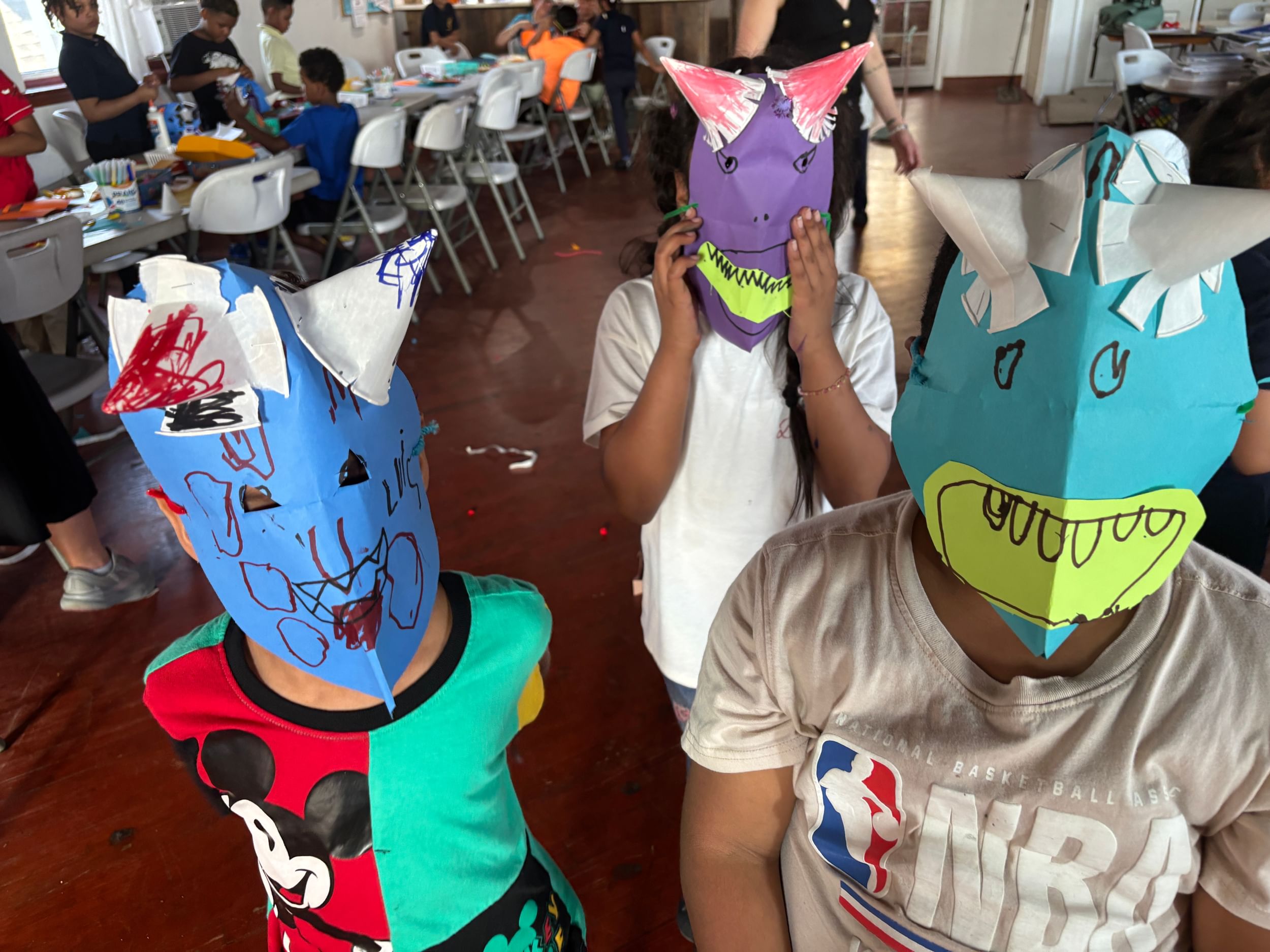 Three children in blue, purple and teal paper masks with handmade paper horns.
