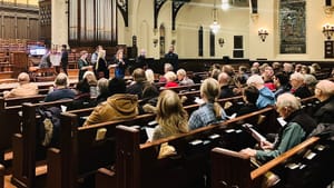 Photo taken over the audience in the pews shows the singers performing on the well-lit chancel.