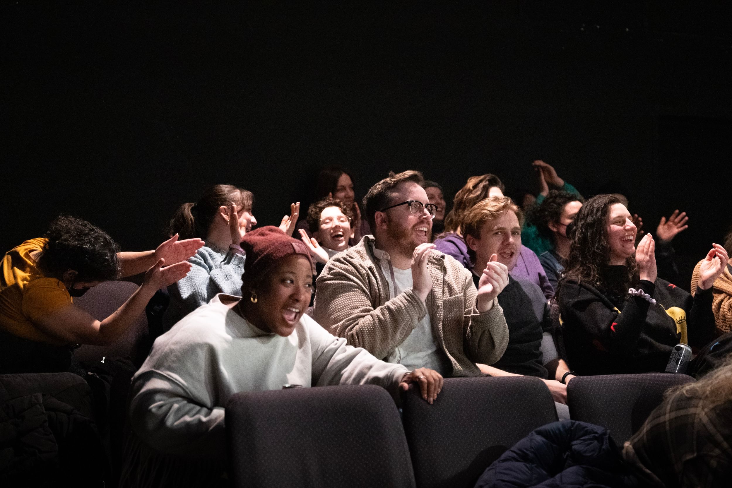 View of an audience in a small theater laughing and clapping uproariously.
