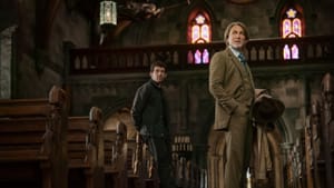 Craig, in a snazzy brown suit, stands in a small, ornate Catholic nave with wooden pews, stone arches, and stained glass.