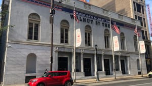 The Walnut Street Theatre today. It has a gray exterior with columns and large windows. American flags fly on poles in front