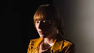 Werbeloff, a white woman with auburn hair and yellow leather jacket, sits with hands clasped to her chest, a worried gesture