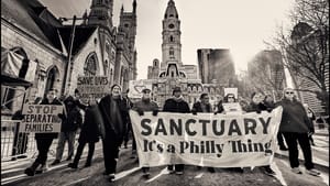 A multiracial group of protestors carry a large sign reading “SANCTUARY It’s a Philly Thing” outside City Hall.
