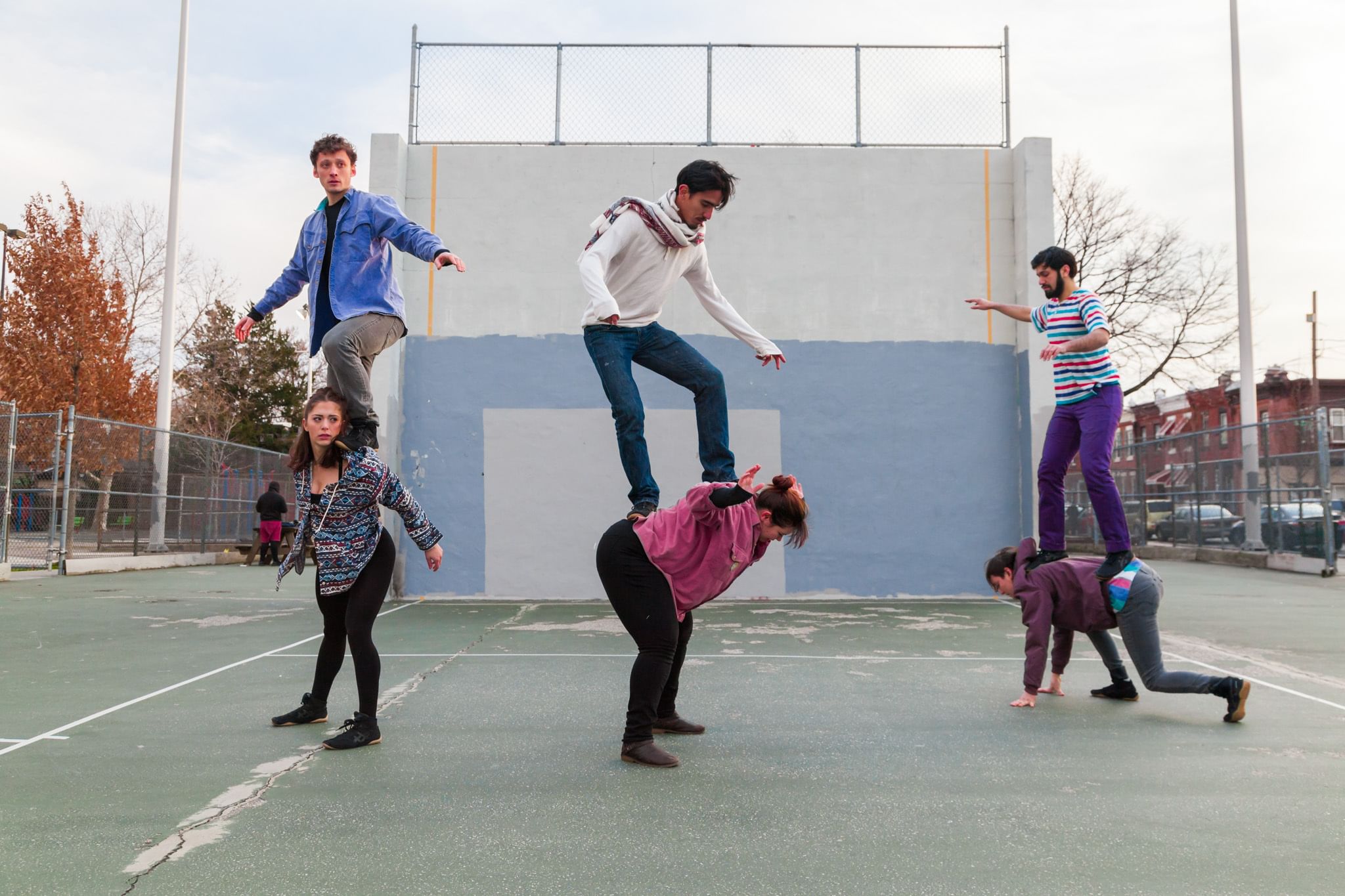 Six circus artists in a playground area, three standing on the other dancers' shoulders and back