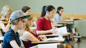 A group of young students studying in a classroom, sitting at desks, their attention at open books