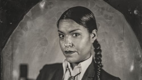 Navajo woman with a braid, black blazer, & bolo tie, in three-quarter pose, looks at the viewer in a black-&-white tintype.