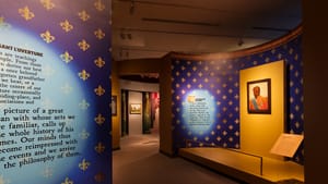 Exhibition view: curving blue-and-gold walls create an inviting path through spotlit wall text and art pieces.