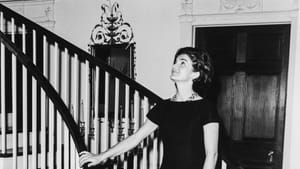 A black & white photo of Kennedy, standing at the bottom of Winterthur’s grand curving stairway, looking admiringly upward