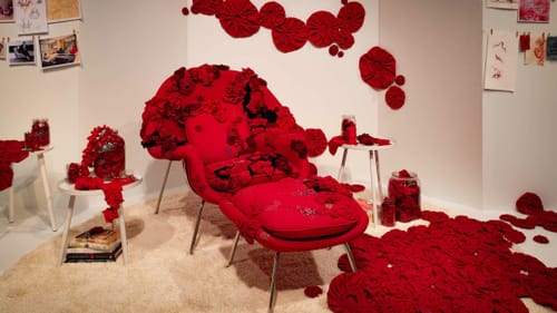 A bright red chair with matching footrest is festooned with organic-feeling, almost floral-looking red textile accents.