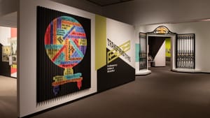Gallery view including the entry with the ironwork described below, and large colorful pleated graphic of the artists’ names