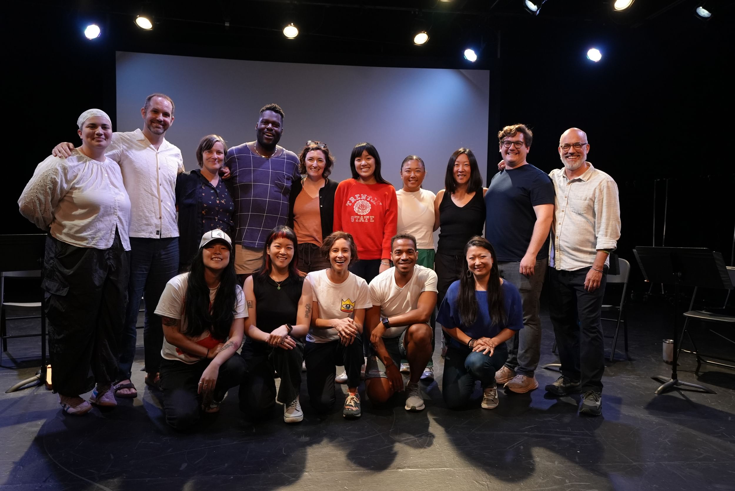 A group cast and crew photo on a warmly-lit stage