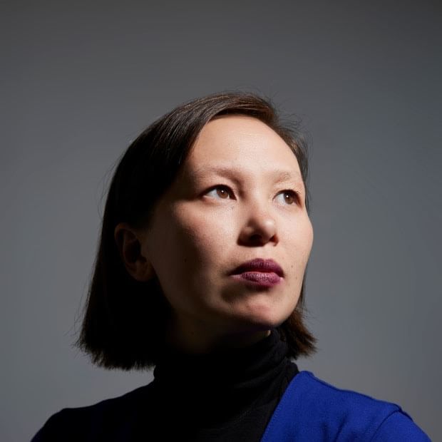 Portrait photo of Woo, from shoulder up, centered. She looks slightly to her left, against a gray backdrop