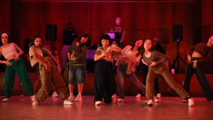 A group of dancers in mid-movement on a stage, a few looking directly at the camera