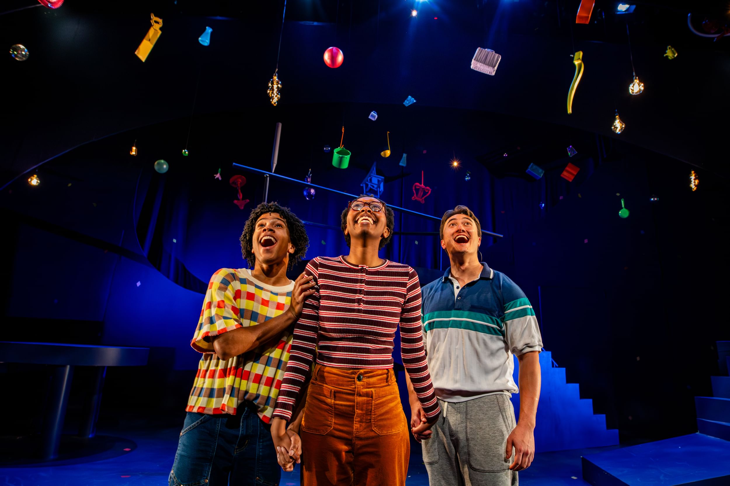 In bright, comfy stripes & plaids, the actors hold hands, looking up with ecstatic smiles at a shower of colorful objects