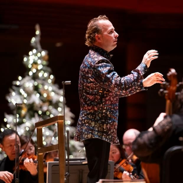 Nézet-Séguin on stage conducting, wearing a festive blazer and a Christmas tree slightly out of focus in background