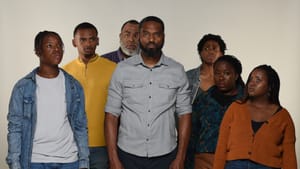 The cast poses together, wearing ordinary clothes, against a beige background, some serious, some sad, some worried.