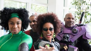 A group of four Black cosplayers in costume poses emphatically, joyfully, in a bright indoor space