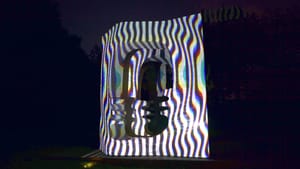 A canvas outdoors at night, trees in the background. Bright lights and distorting, squiggled lines illuminate the canvas.