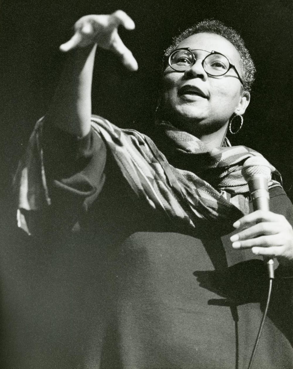 Close-up of hooks speaking out to an audience holding a microphone. Image is in black and white.