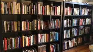Two large black bookshelves packed with hundreds of books in a living room with a hardwood floor.