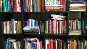 Close-up on 12 square black shelf cubbies crammed with all types of books, some new and some worn.