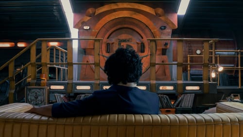 Spike sits on a couch, his back facing the camera, as he looks towards a closed door in the spaceship