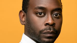 A headshot of Ijames, a Black man in his late 30s. He looks with gentle dignity at the camera & wears a white collared shirt.