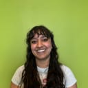 Photo of Chhaya, a smiling Indian woman with long dark hear, wearing a t-shirt, standing against a green background.