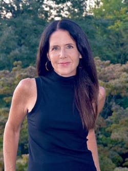 Headshot of Elise Juska, a white woman in a black tank top with long brown hair and hoop earrings. She smiles slightly.