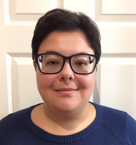 Emily is a white woman with short brown hair and glasses, wearing a dark shirt.