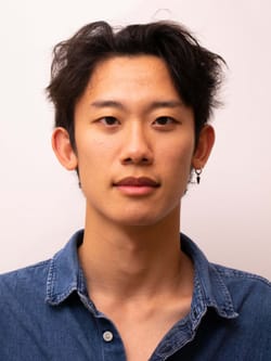 Harrison, an Asian man, looks straight at the camera, wearing a blue button-down, with a relaxed slightly smiling expression