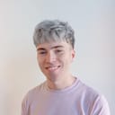 Headshot of Jake. He's a young white man with gray hair, smiling and wearing a light-colored tee against a white background.