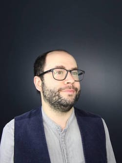 Headshot of Samuel Dunsiger, a white man with a short beard and glasses. He wears a gray shirt with a black vest.