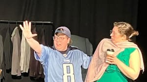 Knight, a white man in a blue jersey and backwards cap, gestures wildly while Fauzer, in a green dress, looks on, surprised.
