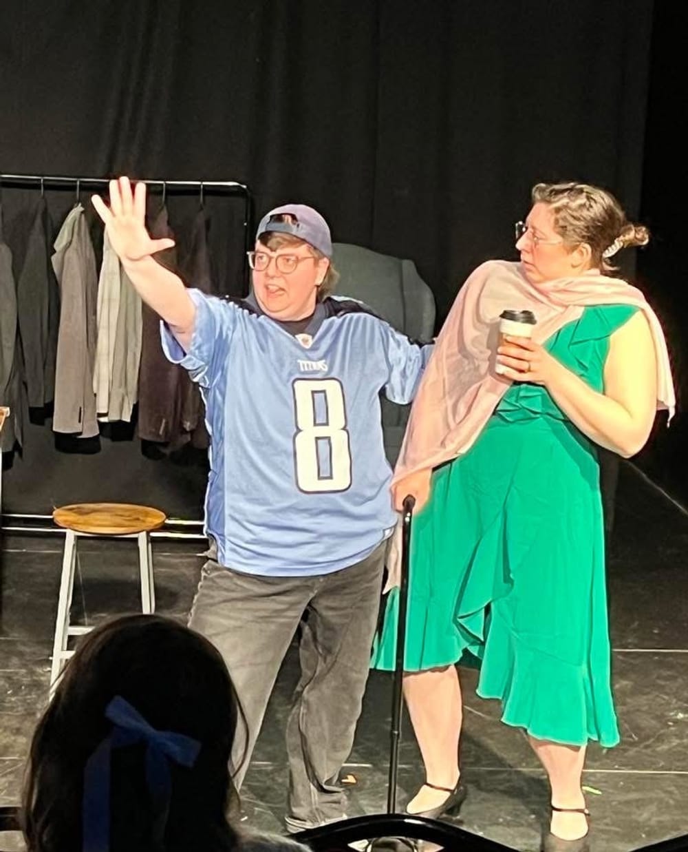 Knight, a white man in a blue jersey and backwards cap, gestures wildly while Fauzer, in a green dress, looks on, surprised.