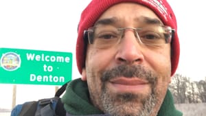 Johnston, a Black man, takes a selfie in front of a city limits sign that reads Welcome to Denton.