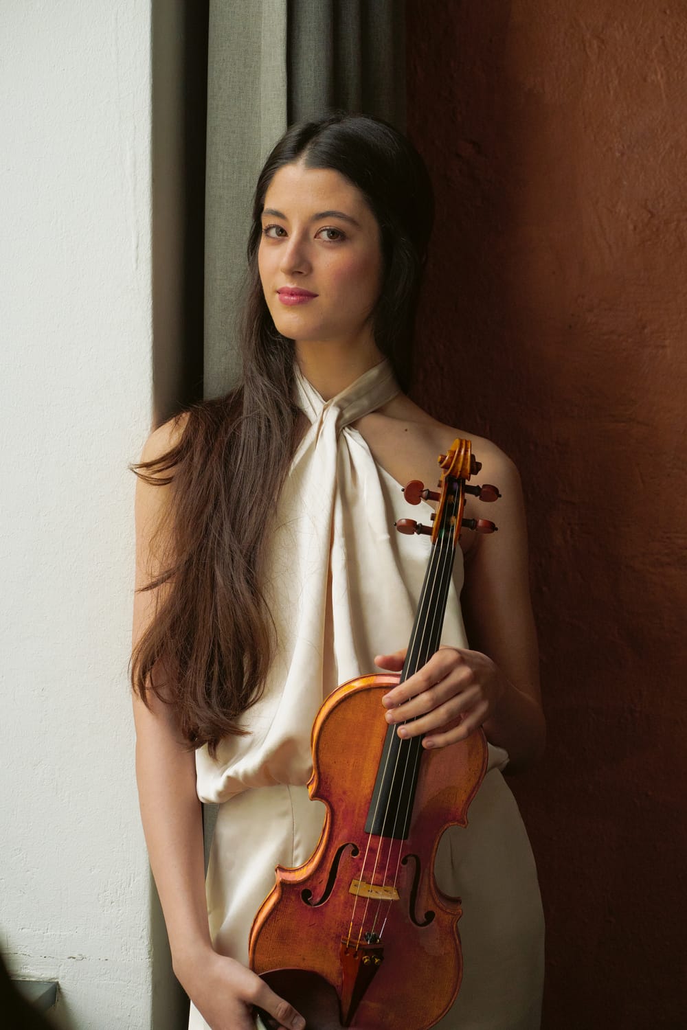 Portrait shot of Dueñas, wearing a white gown and holding a violin.