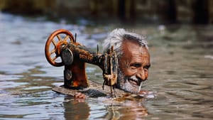 “Tailor Carries His Sewing Machine through Monsoon Waters” (Gujarat, 1983). (Photo © Steve McCurry)