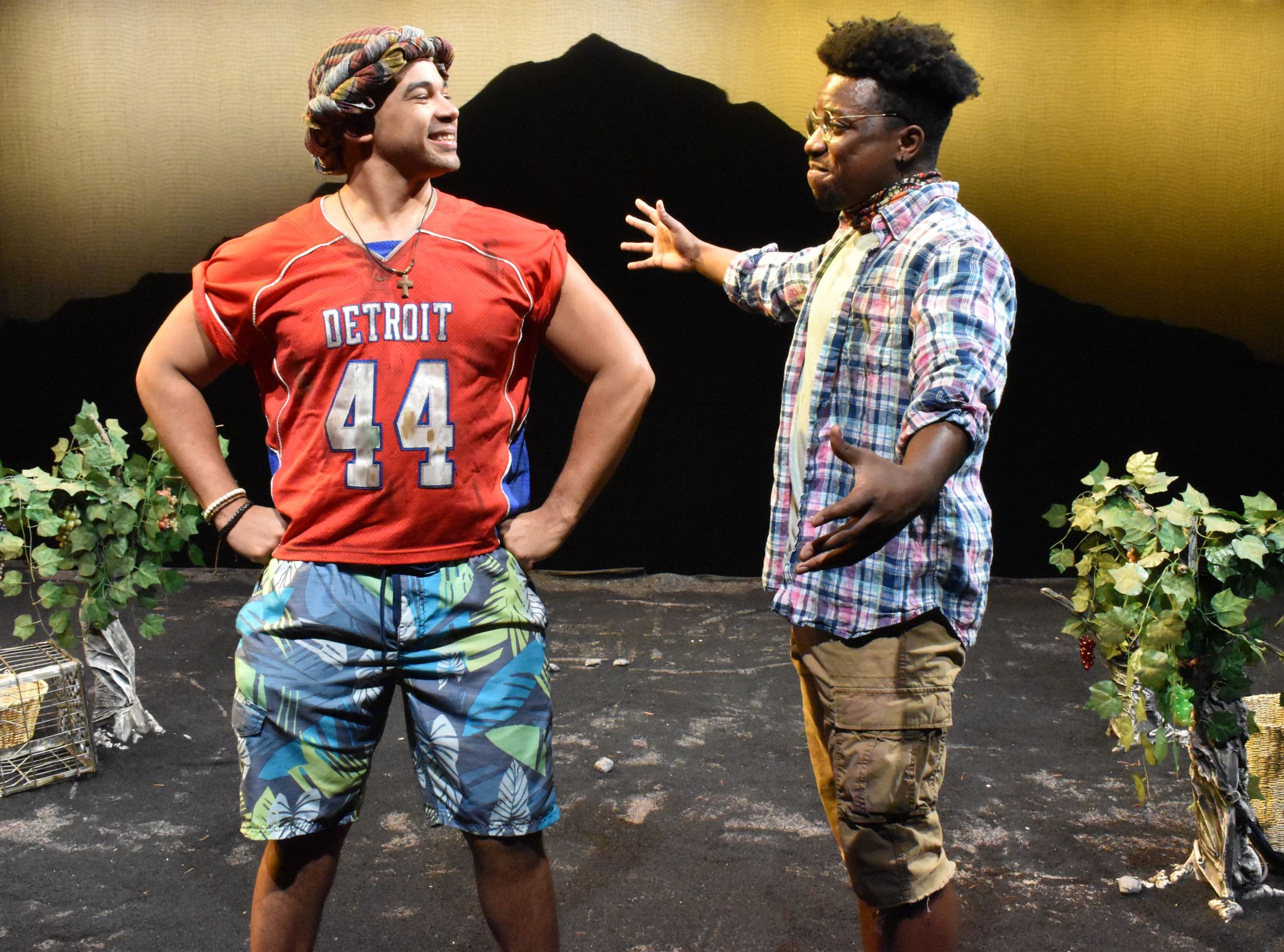 Wallace, smiling with hands on hips, in board shorts & a Detroit football jersey, confronts Foy-Coles, in glasses & plaid.