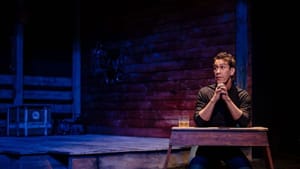 Montano, at right in an empty stable, kneels and clasps his hands at a low table, with a glass of liquor at his elbow.