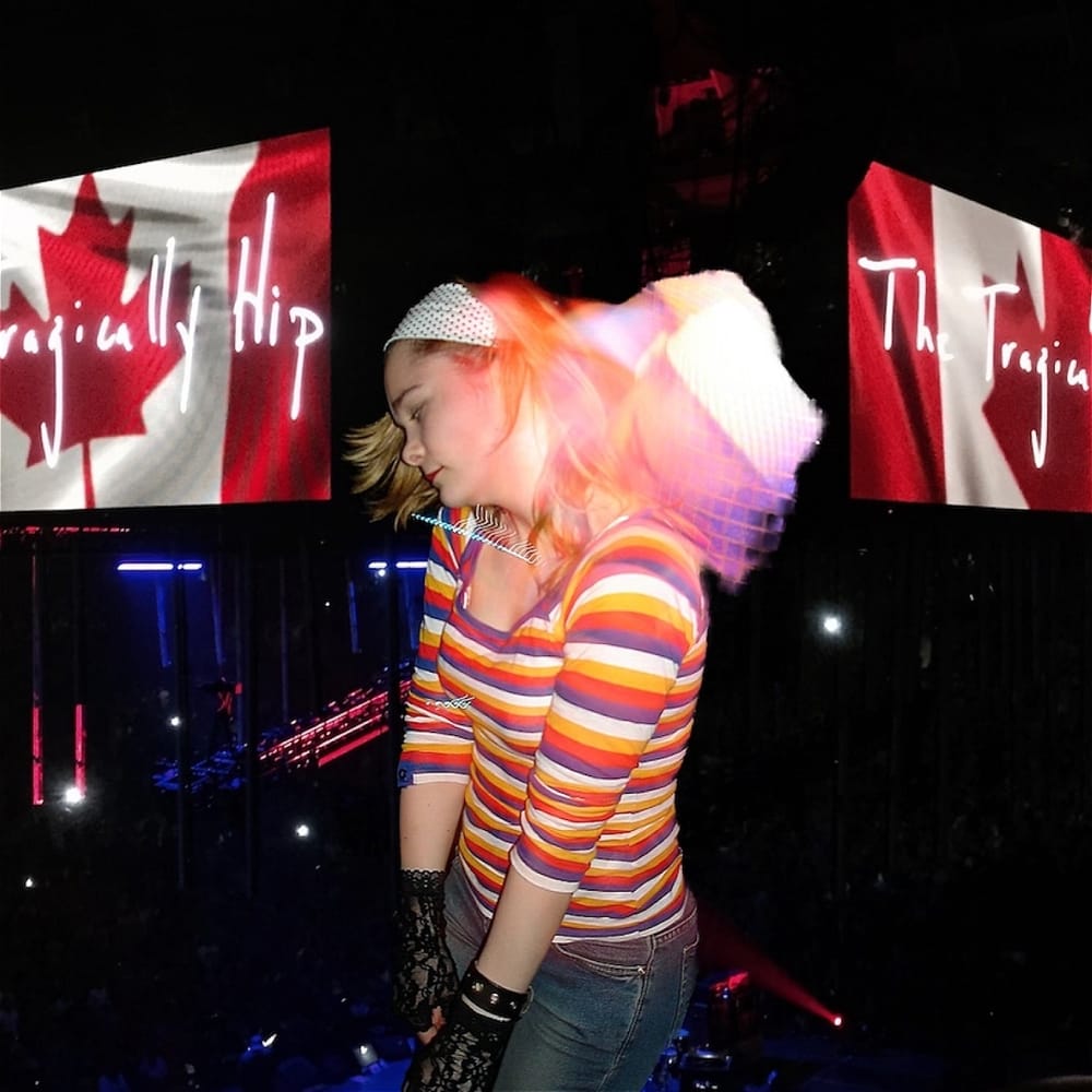 Northeast, in striped shirt, black lace gloves and swinging blond hair, listens to music with the Tragically Hip logo behind