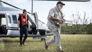 Jose Andres and one other man hurry away from a just-landed helicopter. Andres carries two large aluminum trays of food.